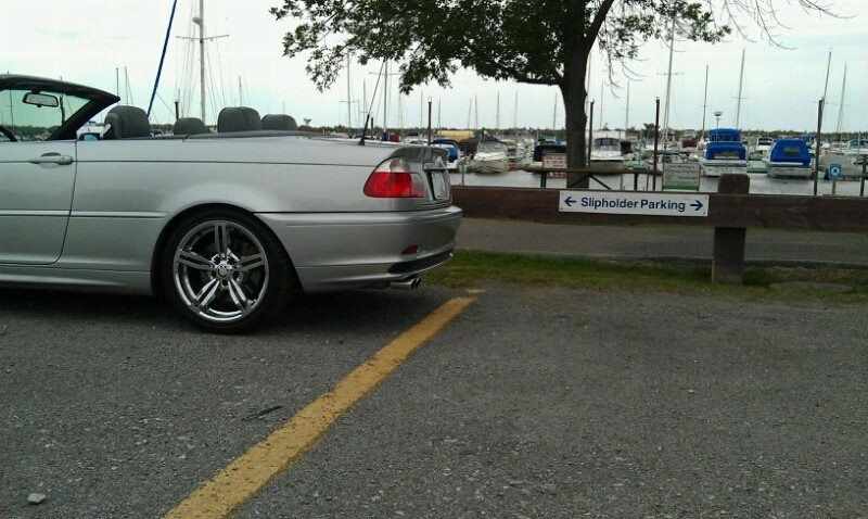 Silver convertible car parked near a marina; cloudy day.
