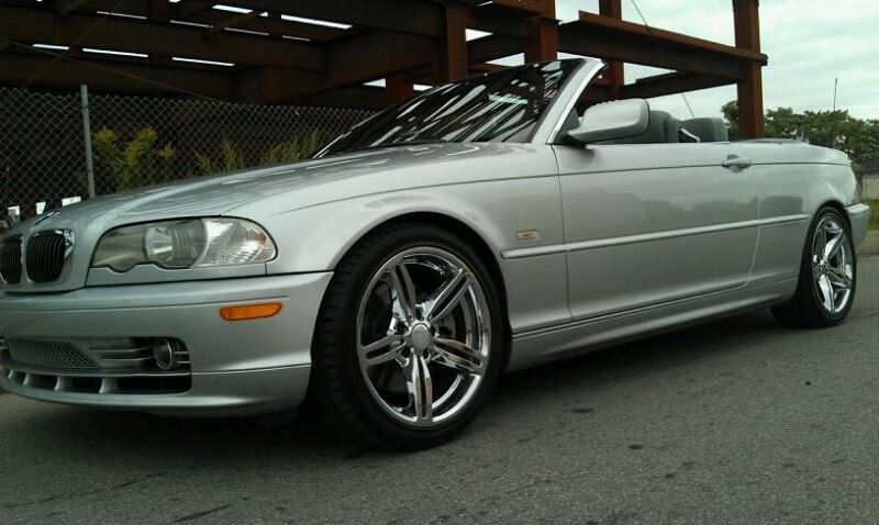 Silver BMW convertible with chrome rims parked on asphalt.