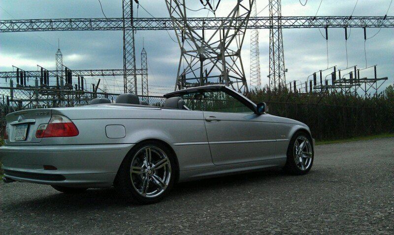 Silver convertible car parked near power lines and equipment on a cloudy day.