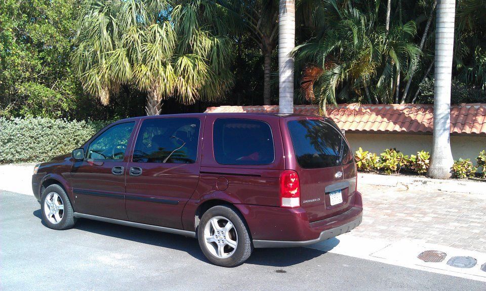 Maroon minivan parked on a sunny street, palm trees in the background.