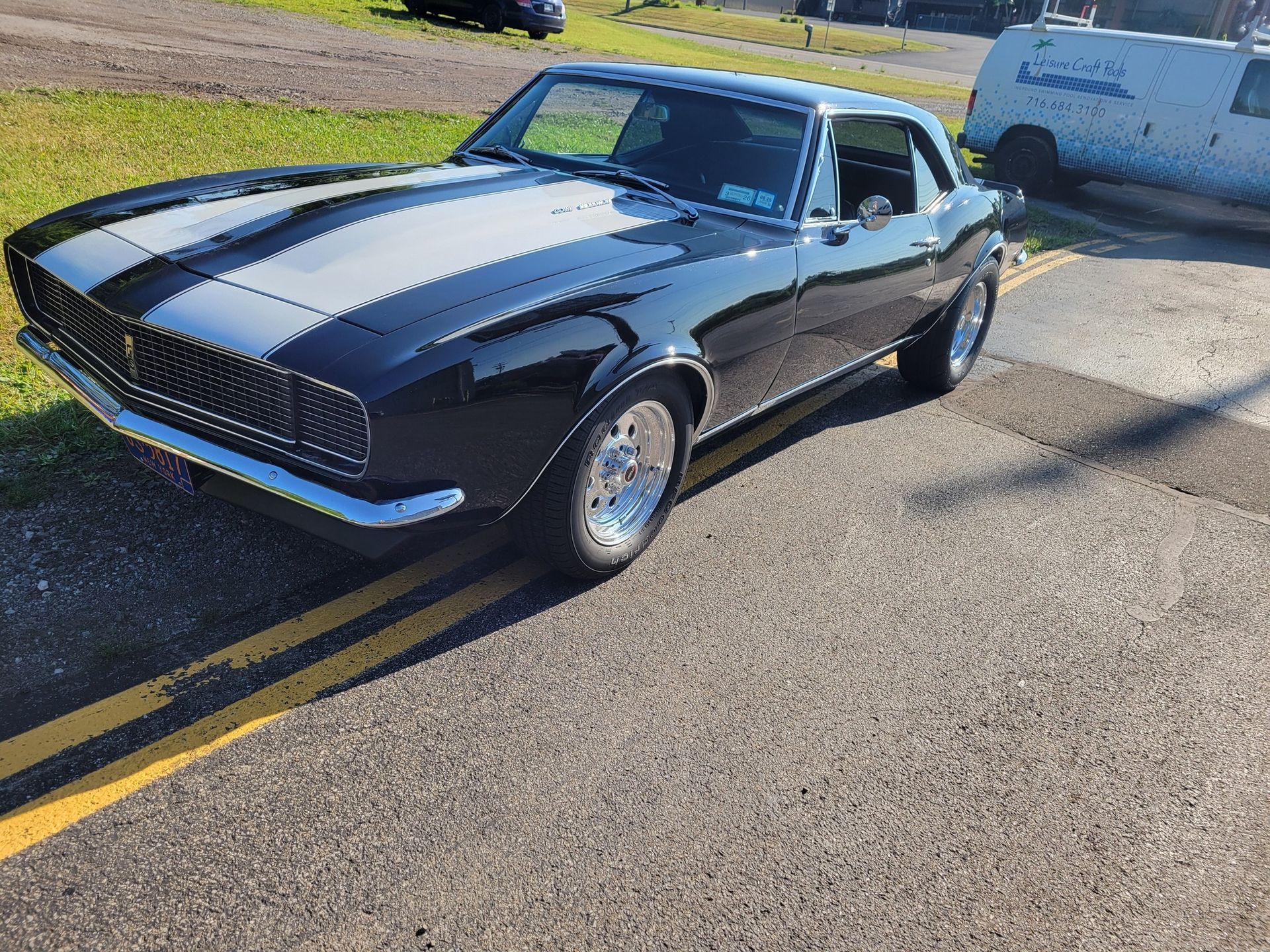 Black classic car with white racing stripes parked on asphalt.
