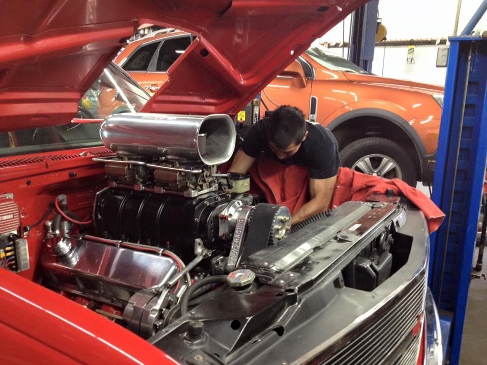 Mechanic working on a red car's engine, hood up, in a garage.