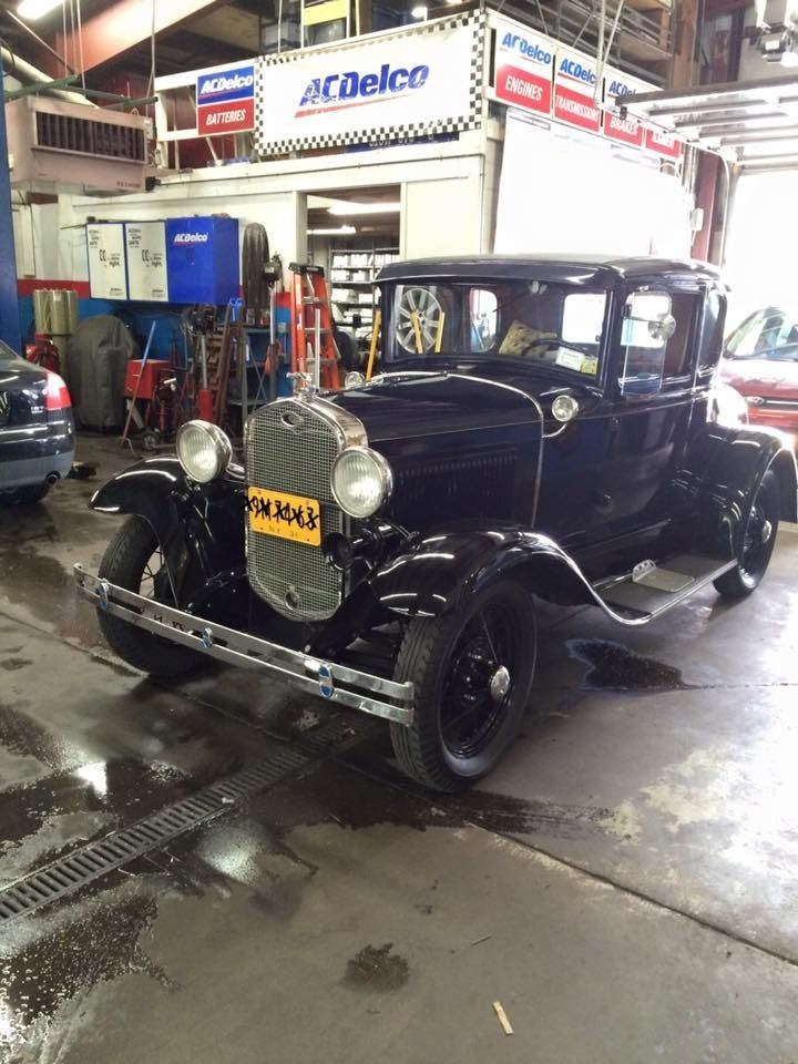 Black classic Ford Model A coupe in a garage, next to a drain.