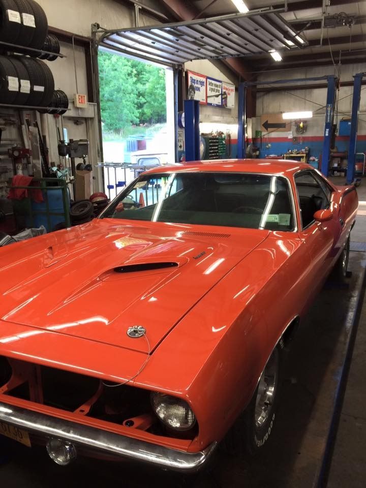 Bright orange classic car inside a garage bay with the door open, showing the road.