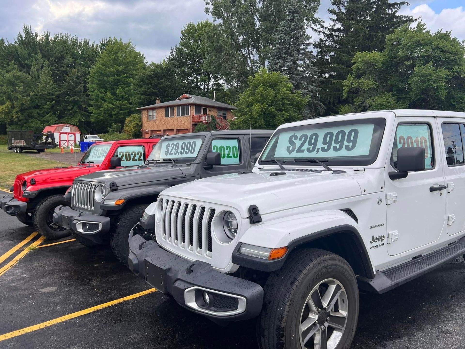 Row of Jeeps in red, gray, and white with price tags, parked in front of a building.