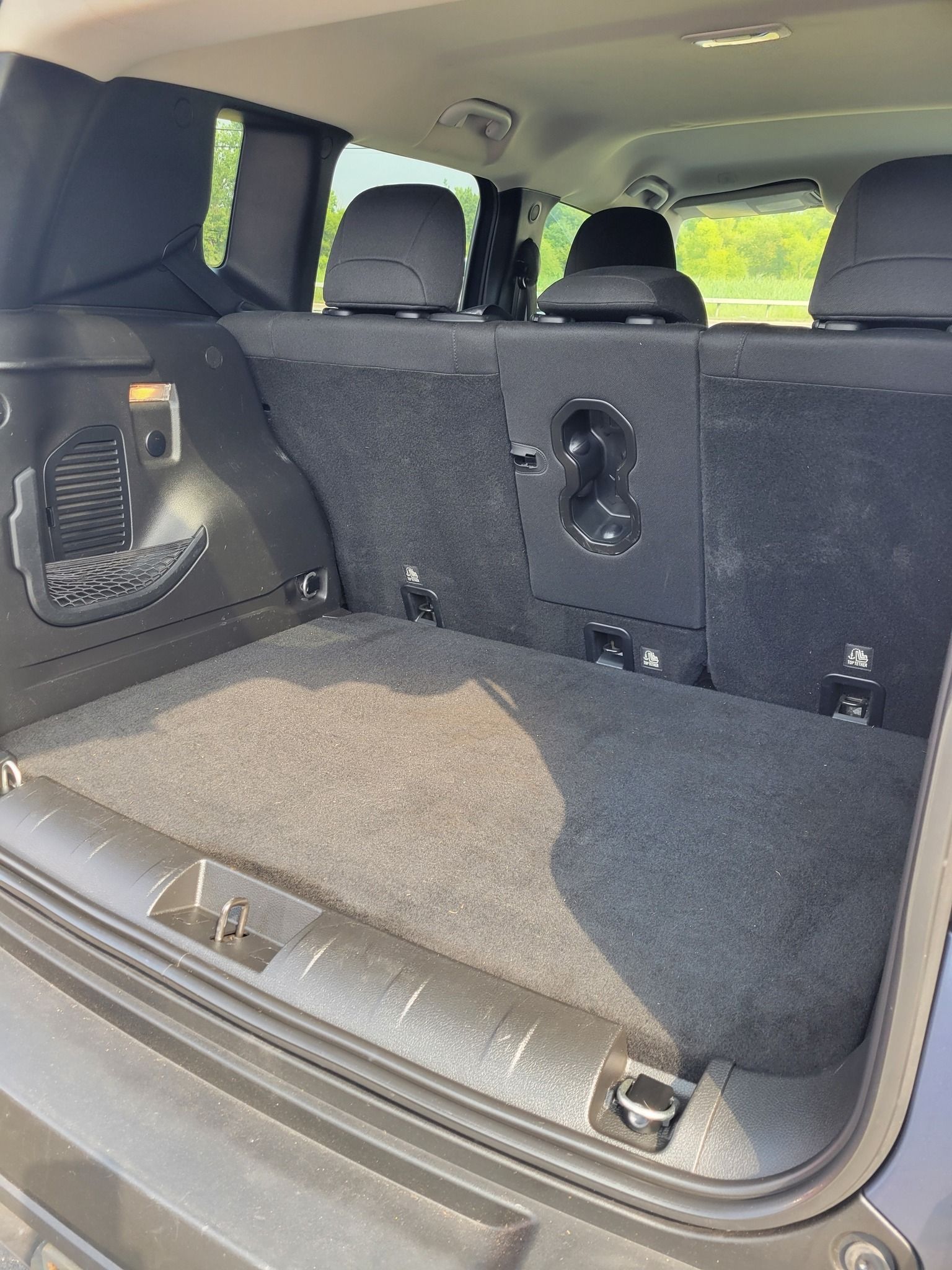 Empty cargo area of a dark-colored SUV, lined with gray carpet. Rear seats folded down.