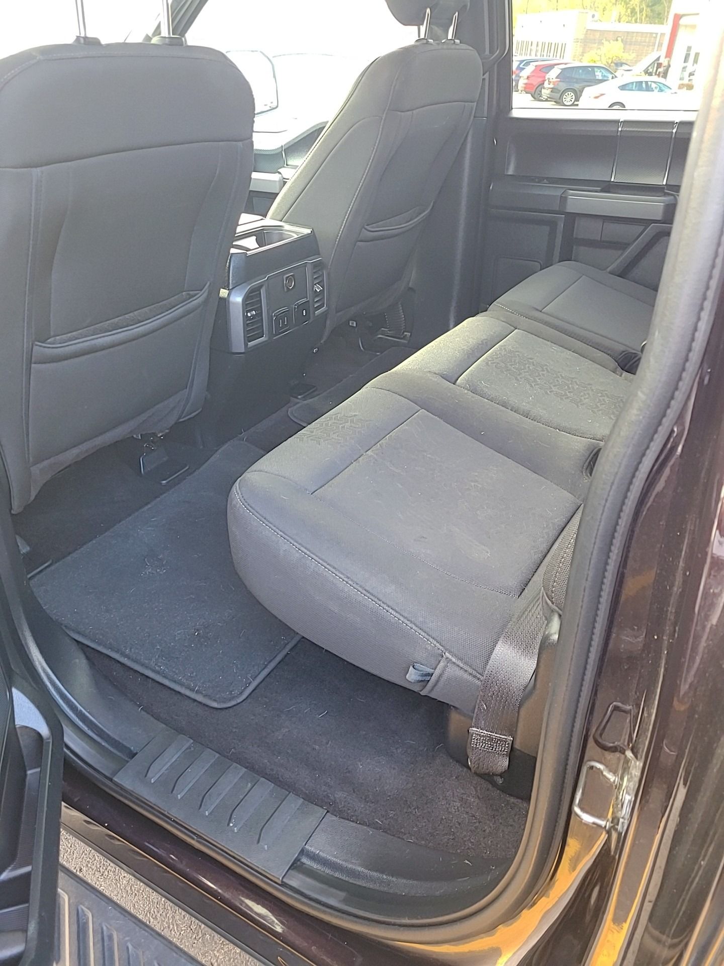 Black Ford truck interior, rear seats folded up, black carpeting.