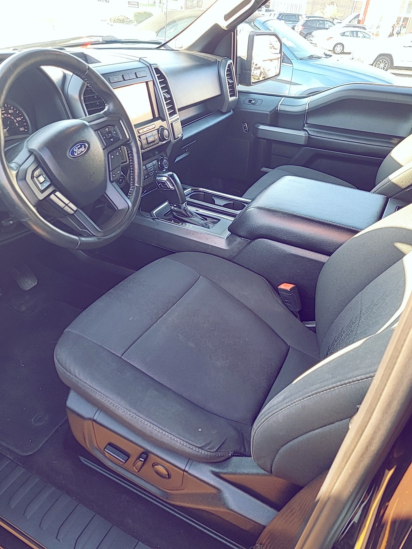 Interior of a black Ford truck with gray cloth seats, steering wheel, and center console.