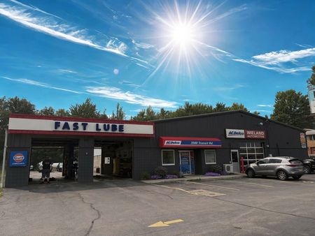 Fast Lube service station with sunny blue sky. Red, white and blue signs. Cars parked outside.