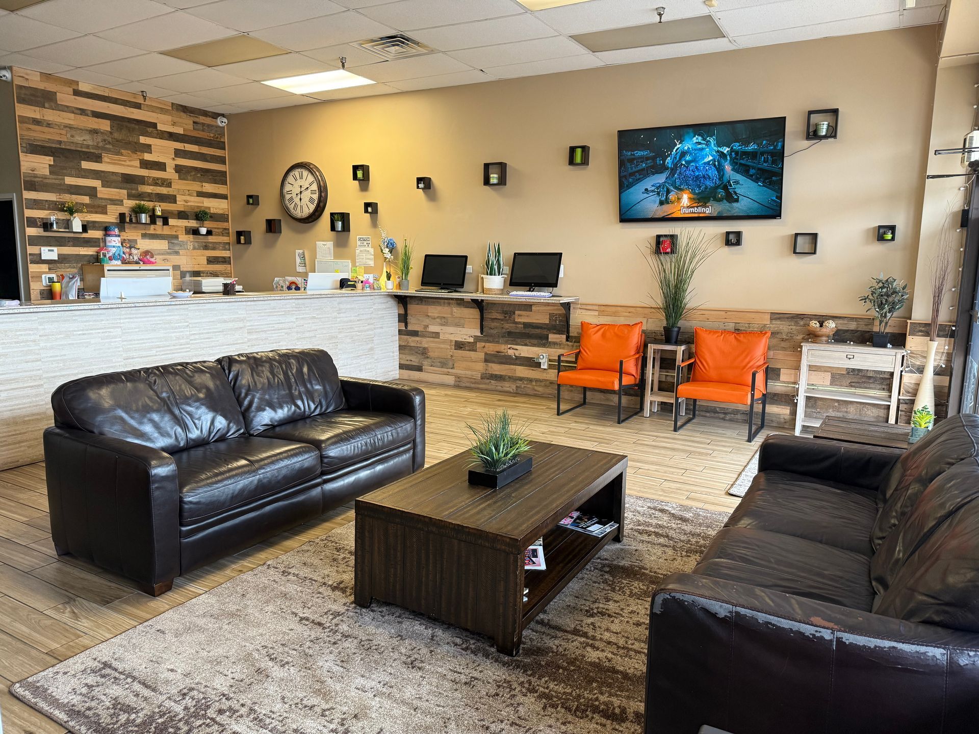 Waiting room with leather sofas, reception desk, TV, and orange chairs.