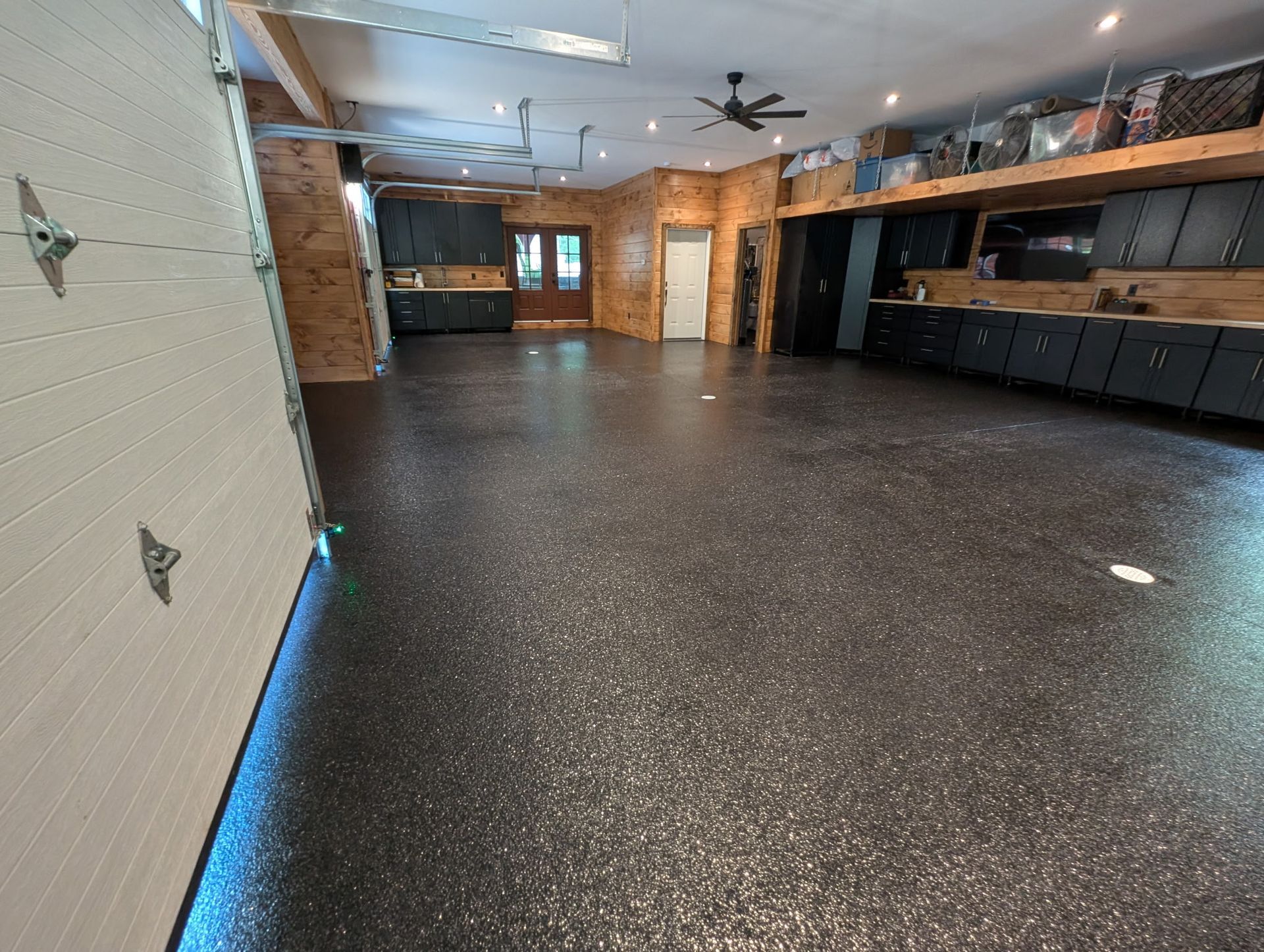 Empty garage with speckled black floor, brick walls, and dark cabinets along one side.