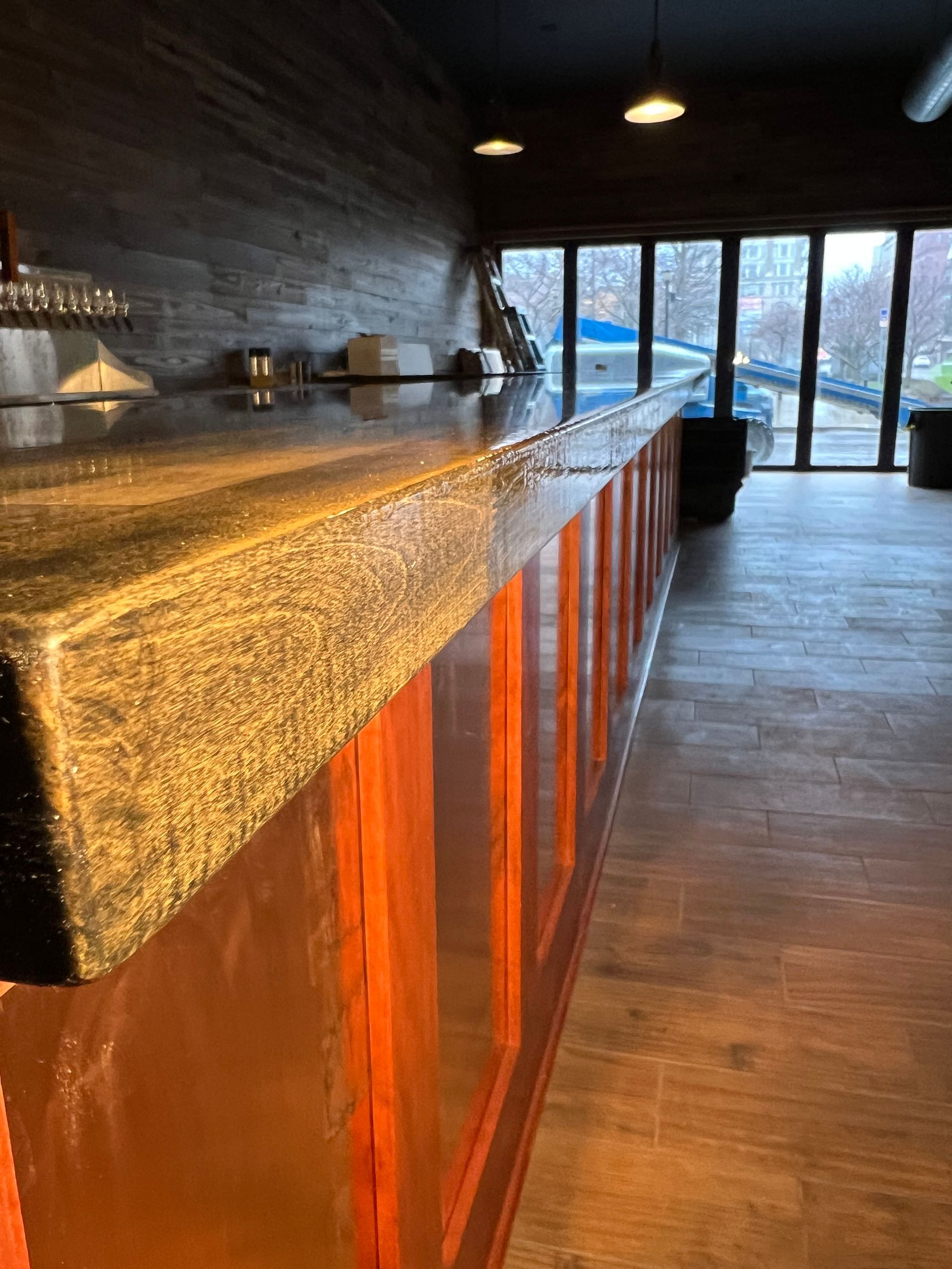 Long wooden counter with copper-toned cabinets in a dim modern room, windows overlooking the outdoors