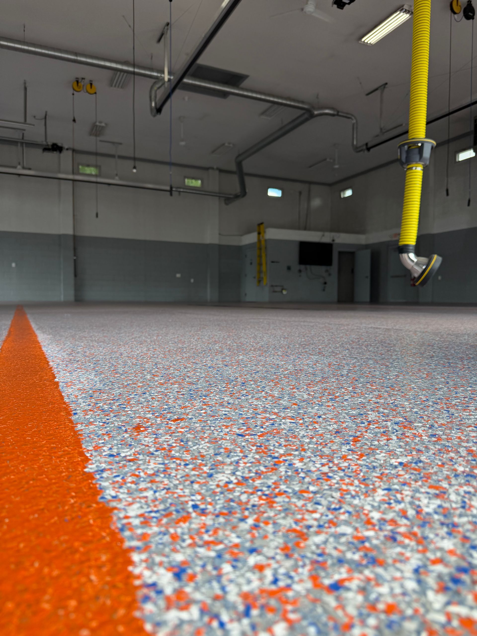 Empty industrial room with speckled epoxy floor and orange safety line, viewed from ground level