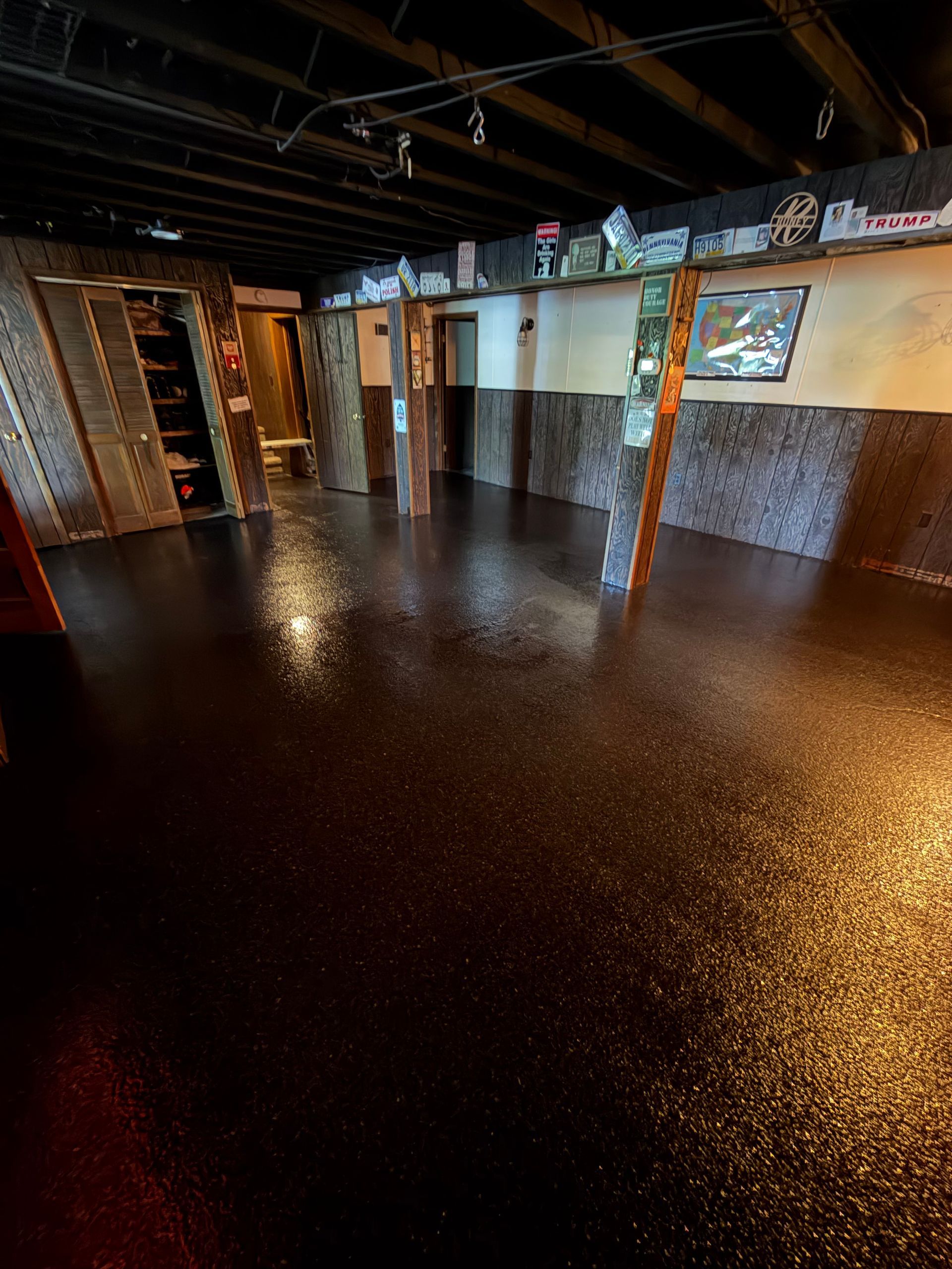 Empty indoor room with dark speckled floor, exposed ceiling beams, and a bar area along the back wall