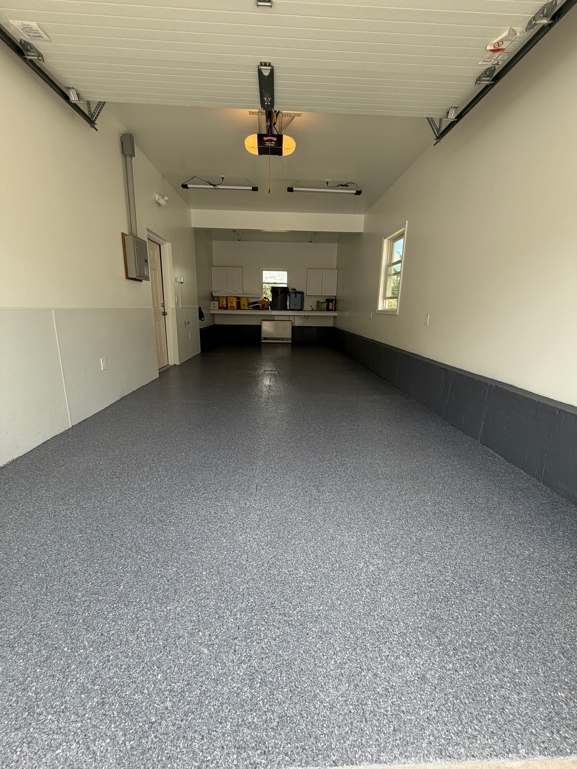 Empty garage with speckled gray floor, white walls, and a workbench at the back.