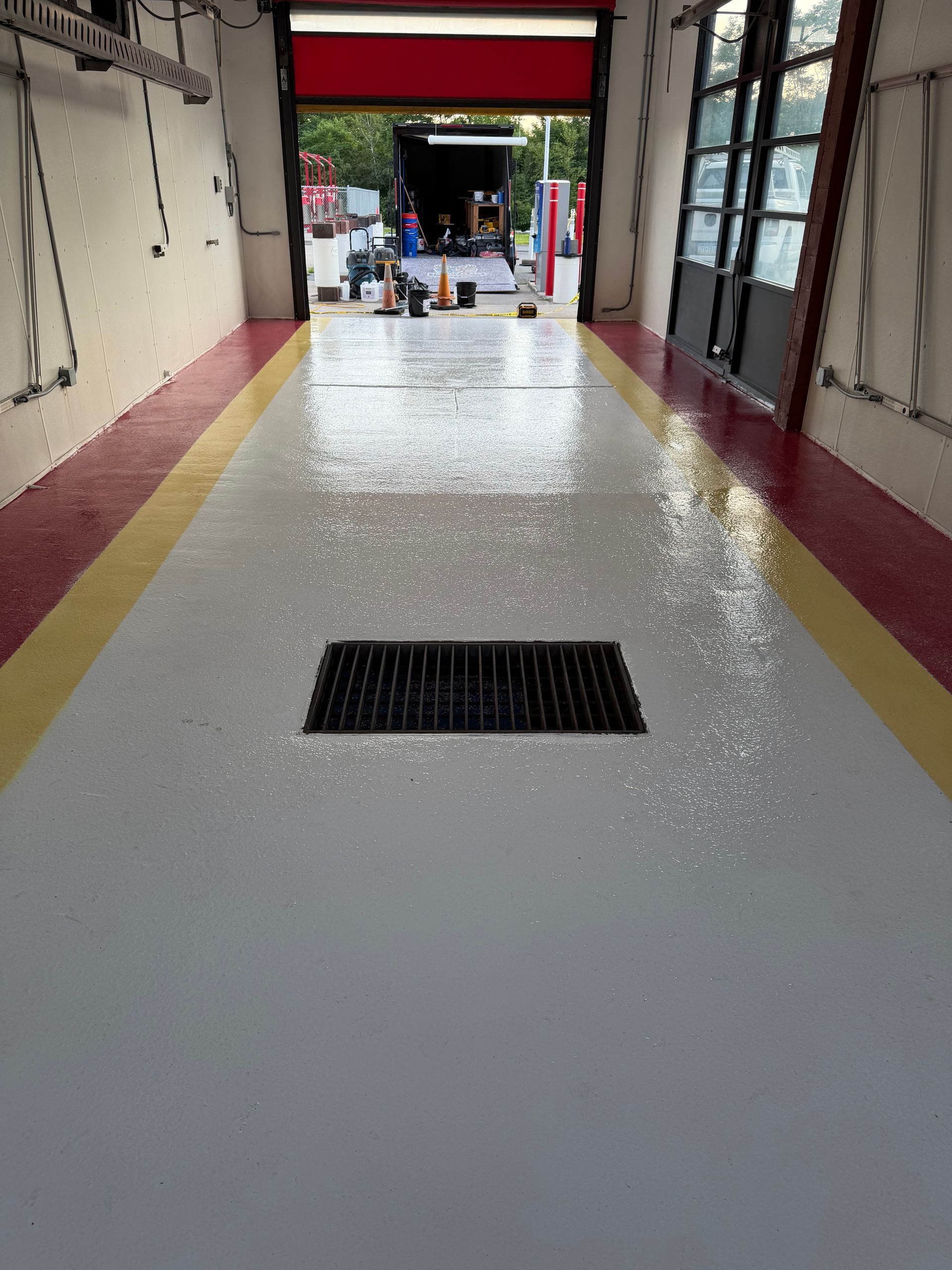 Long indoor hallway with a glossy floor and a black drain grate, opening to a bright outdoor area.
