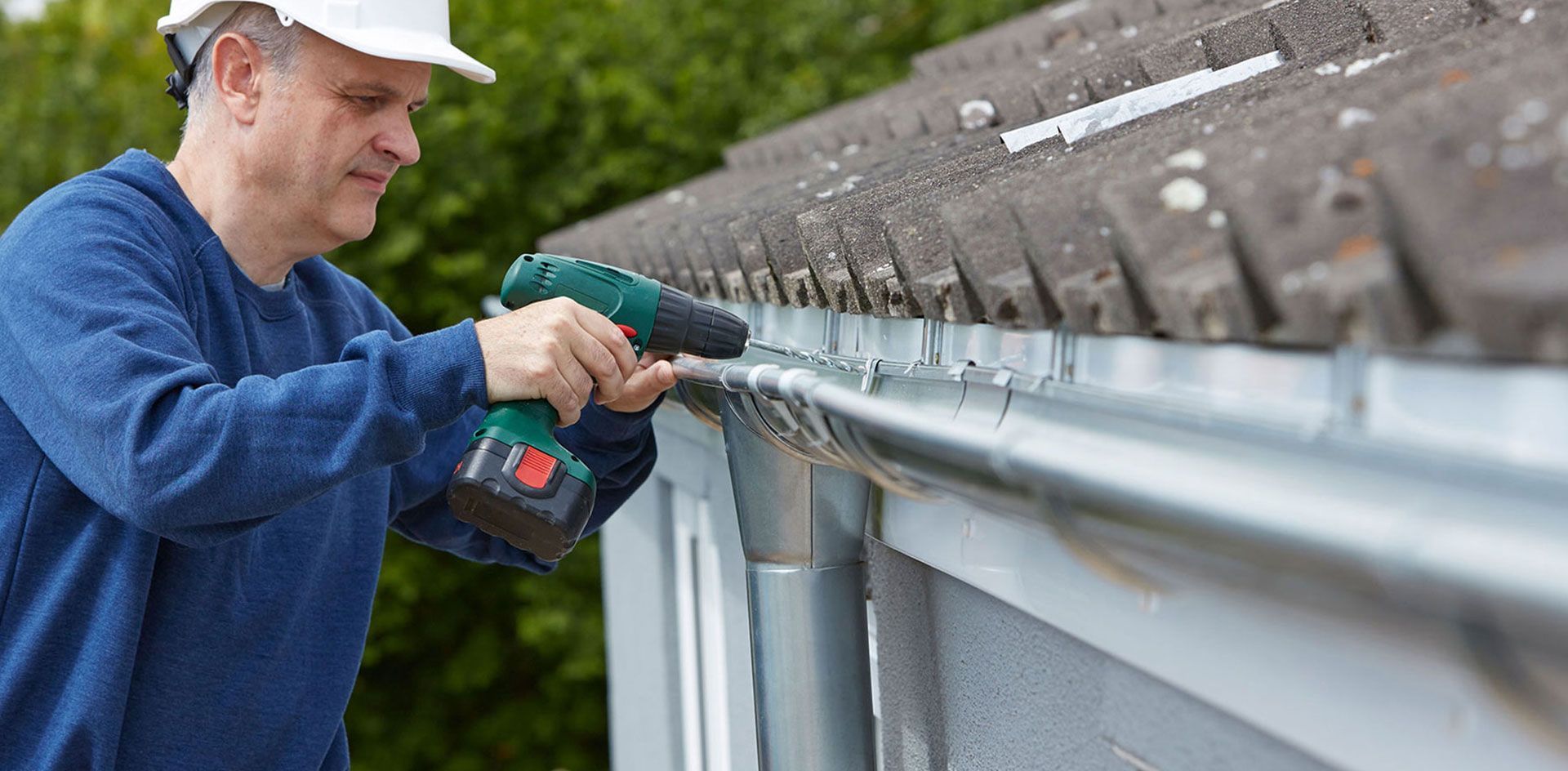 Worker using a drill to clean or install guttering along a roof edge