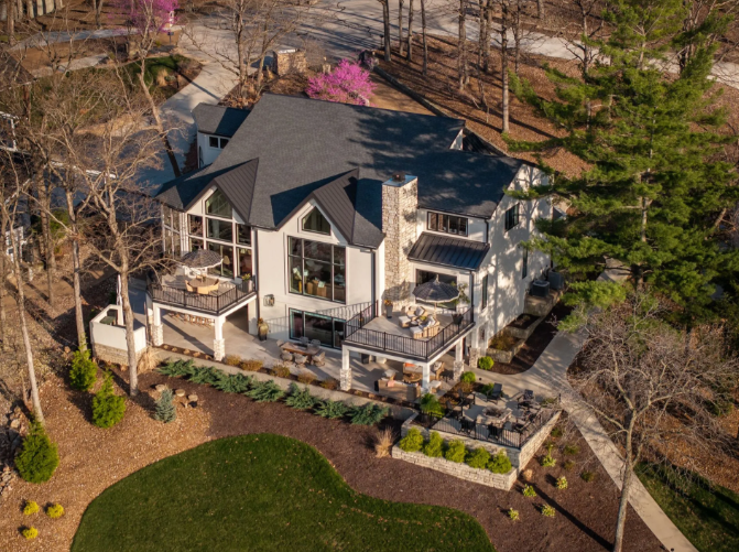 Aerial view of a large stone house with a dark roof, surrounded by a landscaped yard and leafless trees.