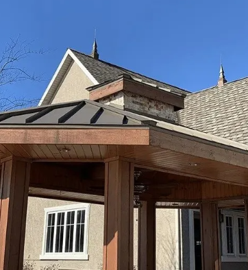 Exterior of a house with a covered porch, shingled roof, and clear blue sky