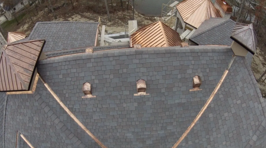 Aerial view of gray shingled rooftops with tan triangular dormers and chimneys.