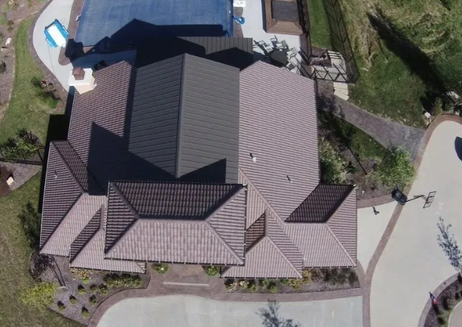Aerial view of a large house with dark shingle roof, driveway, and landscaped yard.