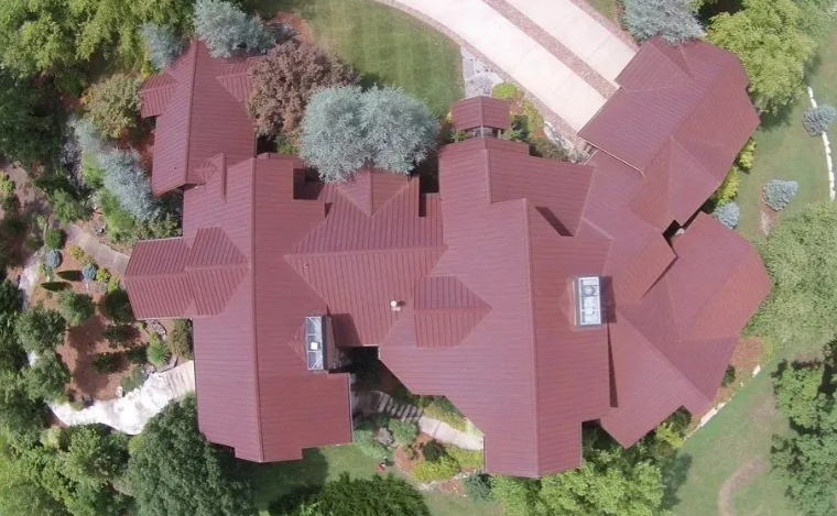Aerial view of a large red-roofed house surrounded by trees and a curved driveway.