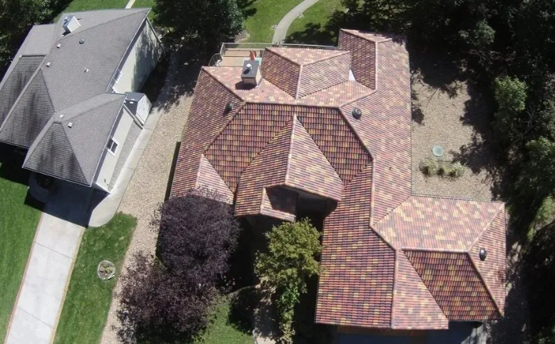 Aerial view of two houses with gray and red roofs beside a green lawn and trees