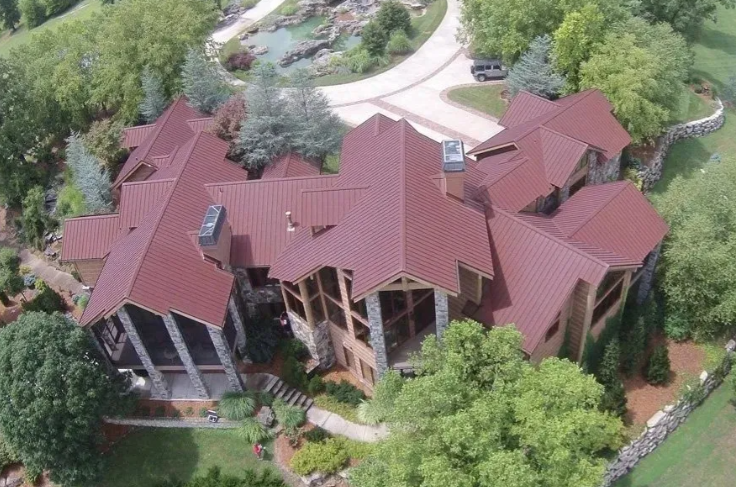 Aerial view of a large house with a red roof surrounded by trees and landscaped grounds