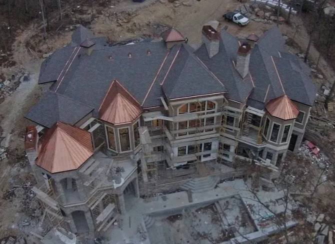 Aerial view of a large house under construction with gray roofing and copper-colored turret tops.