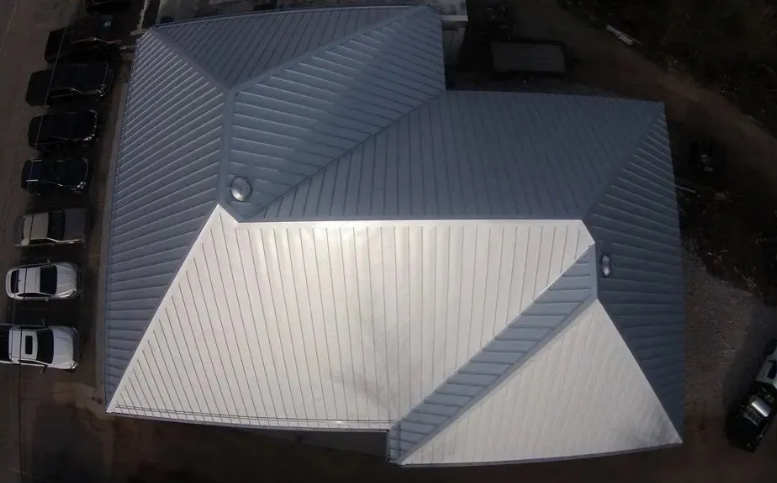 Aerial view of a building with a light metal roof and several parked cars around it.