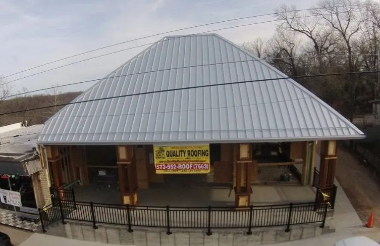 Single-story building with a gray metal roof and front porch, with a yellow sign above the entrance.