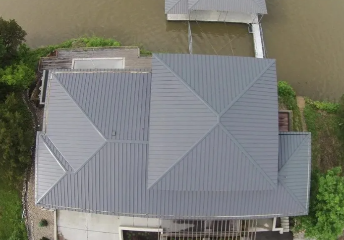 Aerial view of a gray-roofed house beside a canal or river, with trees around it.