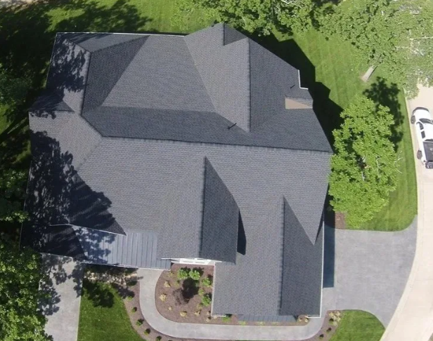 Aerial view of a house with a dark gray roof, driveway, and landscaped yard.