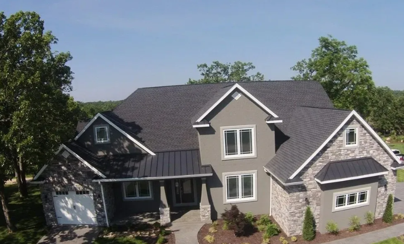 Large modern house with gray shingle roof, stone exterior, and a covered front porch surrounded by trees