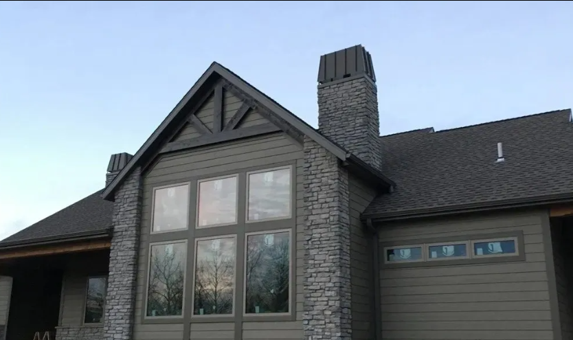 Modern house exterior with gray siding, large windows, and a stone chimney under a blue sky