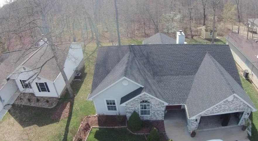 Aerial view of two houses with gray roofs and a tree-lined yard in a suburban neighborhood