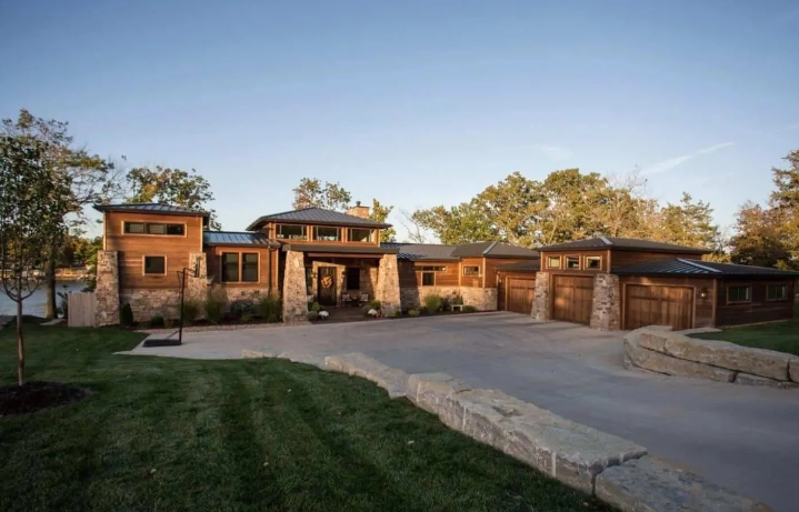 Modern single-story house with wooden accents, large driveway, and green lawn at sunset