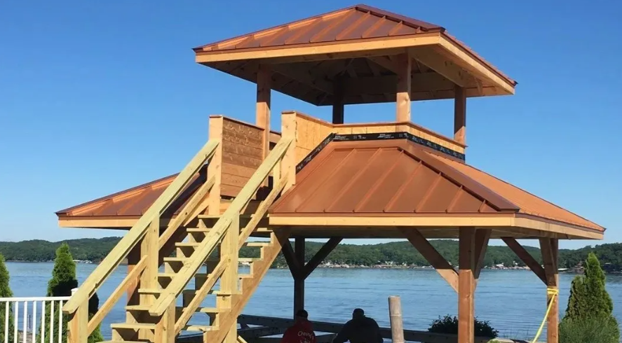 Wooden lakeside gazebo with stairs and a red roof under a blue sky