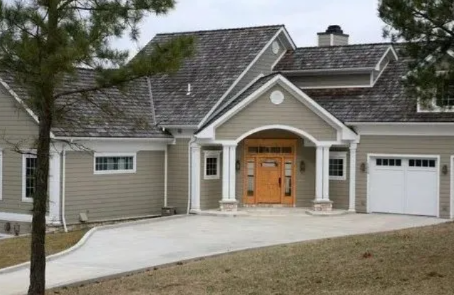 Suburban house with gray siding, arched entry, double wooden doors, and an attached garage