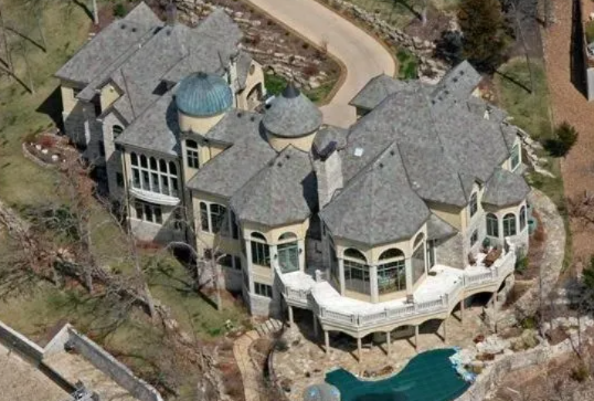 Aerial view of a large gray-roofed mansion with a swimming pool and curving driveway