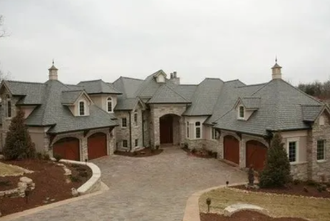 Large stone mansion with multiple garage doors, arched entryways, and a circular driveway