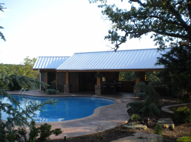 House with metal roof beside a swimming pool, surrounded by trees and landscaping