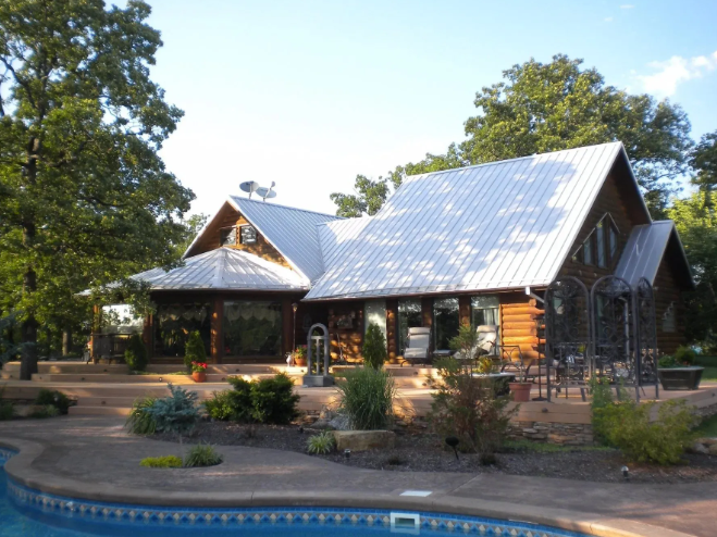 House with metal roof and garden beside a pool in a wooded yard