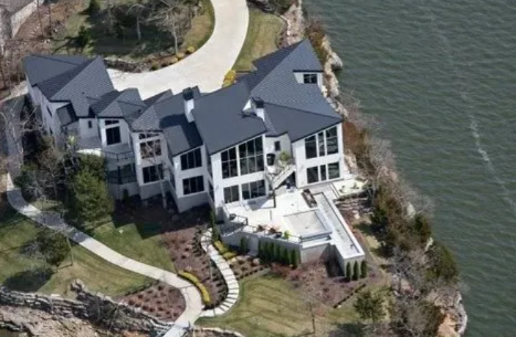 Aerial view of a large gray waterfront house with a patio and curved walkway by the water