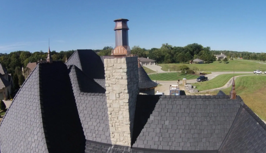 Slate-roofed building with stone chimney overlooking a green golf course on a sunny day