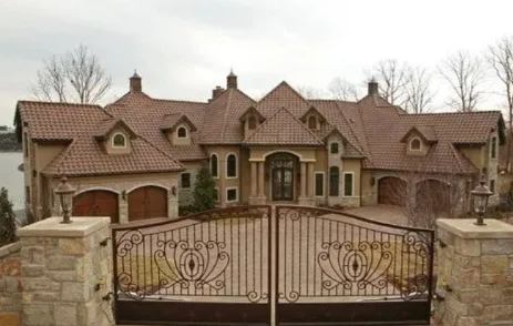 Large stone mansion with ornate gate and circular driveway under bare trees