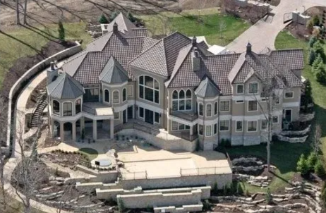 A large stone mansion with multiple gables and balconies, seen from above in a wooded setting.