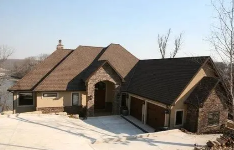 Large tan and dark brown house with snow-covered driveway and roof, viewed from the front-left angle