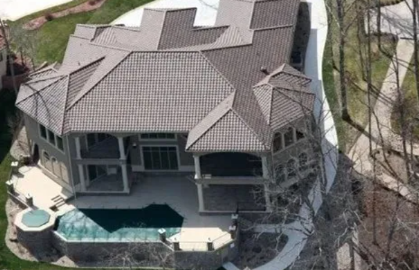 Aerial view of a large house with a tiled roof, screened porch, and backyard pool surrounded by trees
