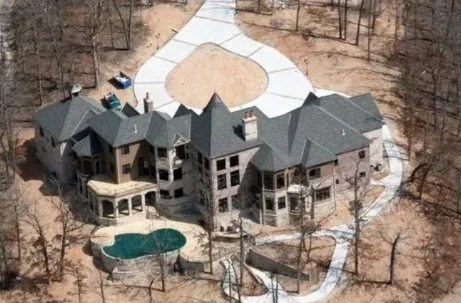 Aerial view of a large house with a pool and circular driveway surrounded by trees